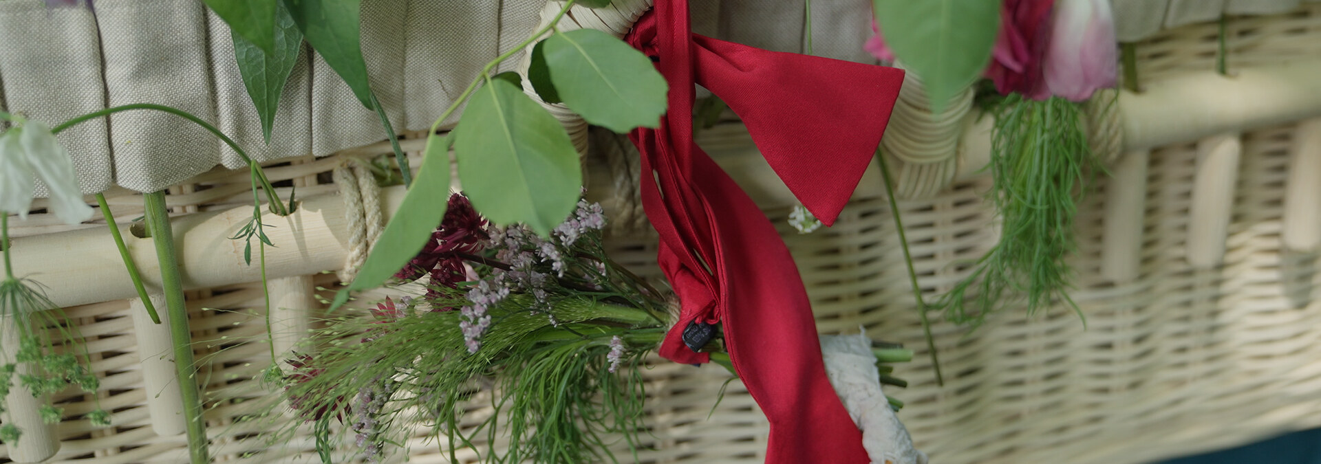 Rood lint en bloemen op een rieten uitvaartkist.